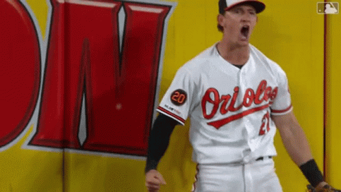 A Baseball Player Wearing An Orioles Uniform Is Standing In Front Of A Yellow Wall . GIF
