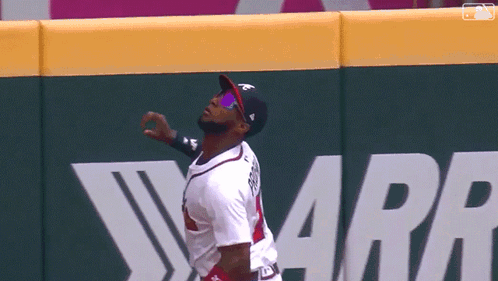 A Baseball Player Wearing Sunglasses And A Hat Stands In Front Of A Wall That Says Warr GIF