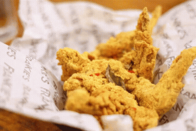 A Basket Of Fried Chicken Is Sitting On A Piece Of Paper That Says ' Fries ' On It GIF