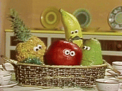 A Basket Of Fruit With Googly Eyes Sits On A Table Next To Cups And Saucers GIF