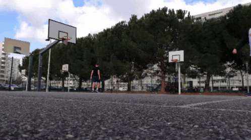 A Basketball Court With A Basketball Hoop And A Few Trees GIF