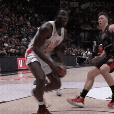 A Basketball Player Dribbles The Ball In Front Of A Sign That Says U On It GIF