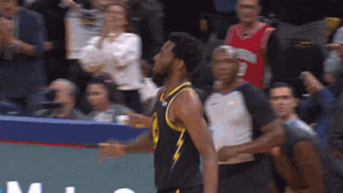 A Basketball Player In A Black Jersey With A Yellow Stripe Stands In Front Of A Crowd GIF