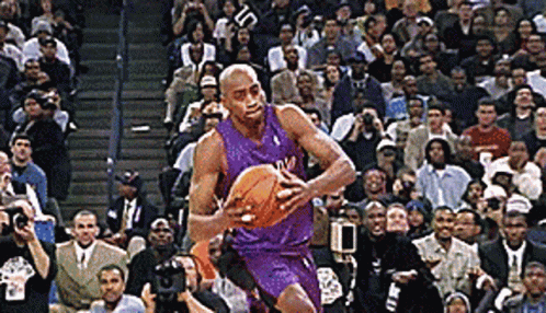 A Basketball Player In A Purple Uniform Is Dribbling A Basketball In Front Of A Crowd GIF