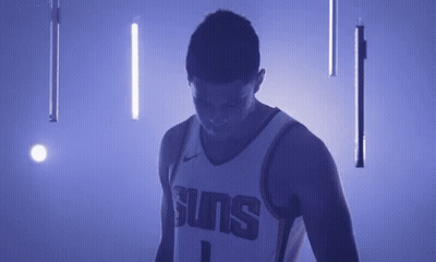 A Basketball Player In A Suns Jersey Is Standing In A Dark Room With Purple Lights . GIF