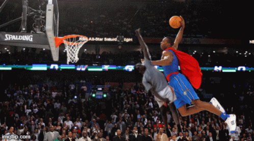 A Basketball Player In A Superhero Cape Jumps In The Air With A Spalding Sign Behind Him GIF