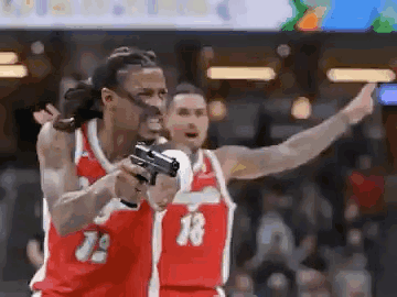 A Basketball Player Is Holding A Gun In His Hand While Another Player Looks On . GIF
