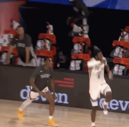A Basketball Player Is Jumping In The Air While Another Player Looks On During A Game GIF