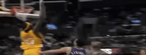 A Basketball Player Is Jumping In The Air While Another Player Tries To Block Him . GIF
