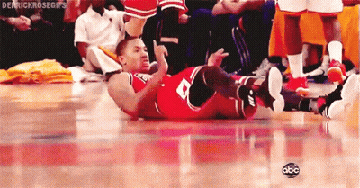 A Basketball Player Is Laying On His Back On The Floor While A Crowd Watches . GIF