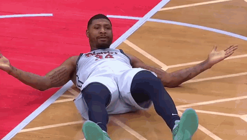A Basketball Player Is Laying On The Floor Of A Basketball Court . GIF