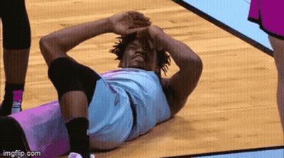 A Basketball Player Is Laying On The Floor With His Head On His Knees . GIF
