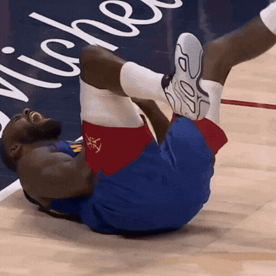 A Basketball Player Is Laying On The Floor With His Legs Up In Front Of A Sign That Says Niche GIF
