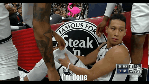 A Basketball Player Is Laying On The Ground With A Steak 'N ' Sign In The Background GIF