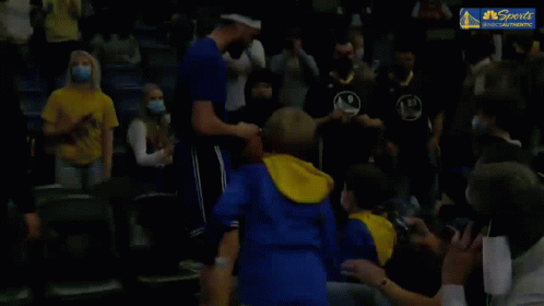 A Basketball Player Is Shaking Hands With A Young Boy In The Stands During A Game . GIF