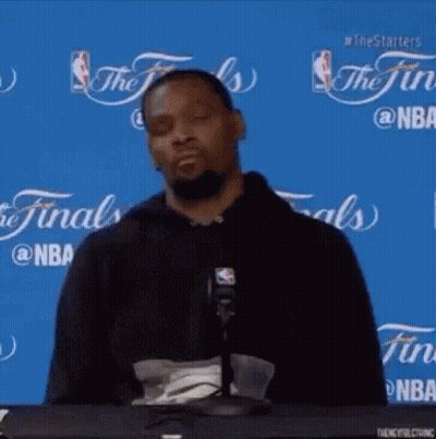 A Basketball Player Is Sitting At A Table In Front Of A Microphone With His Eyes Closed . GIF