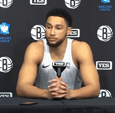 A Basketball Player Is Sitting At A Table With A Microphone In Front Of A Wall That Says Yes GIF