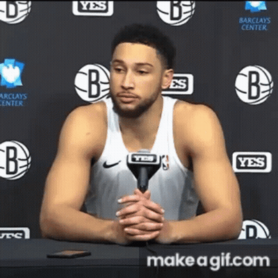 A Basketball Player Is Sitting At A Table With A Microphone In Front Of Him . GIF