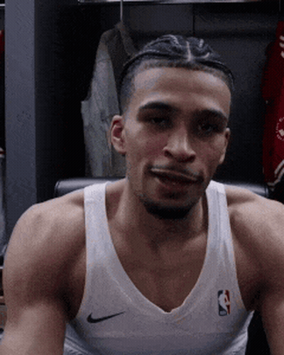 A Basketball Player Is Sitting In A Chair In A Locker Room Wearing A White Nike Tank Top . GIF