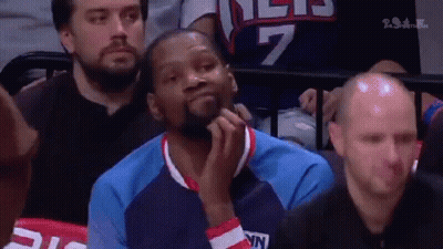 A Basketball Player Is Sitting In The Stands During A Game And Looking At Something . GIF