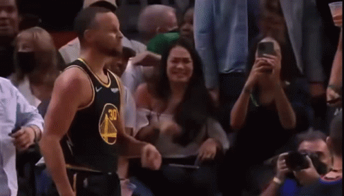 A Basketball Player Is Standing In Front Of A Crowd Of People While A Woman Takes A Picture Of Him . GIF