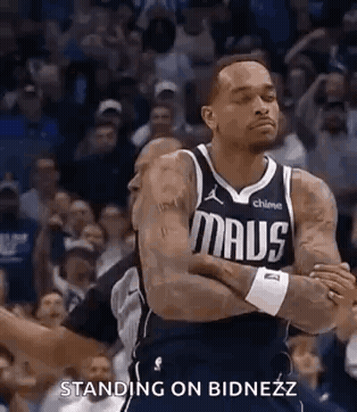 A Basketball Player Is Standing On The Court With His Arms Crossed And A Crowd Behind Him . GIF