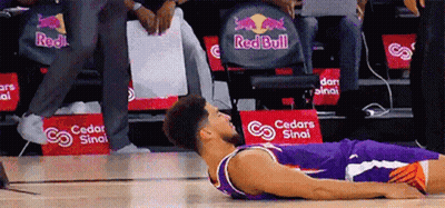 A Basketball Player Laying On The Floor In Front Of A Red Bull Ad GIF