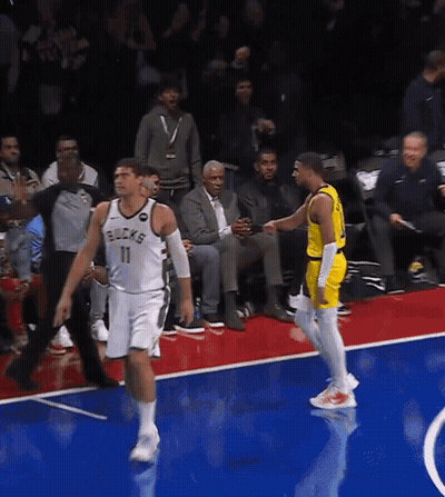 A Basketball Player Wearing A Bucks Jersey Talks To Another Player On The Court GIF