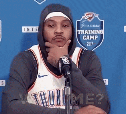 A Basketball Player Wearing A Hoodie Is Standing In Front Of A Microphone With His Hand On His Chin . GIF