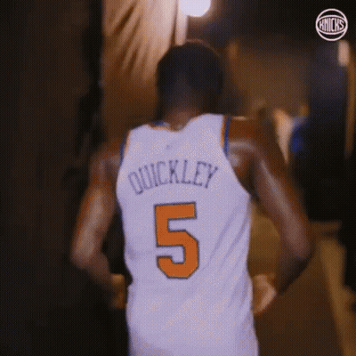 A Basketball Player Wearing A White Jersey With The Number 5 On It Is Walking Down A Hallway . GIF
