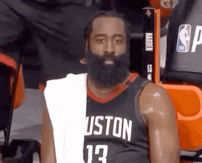 A Basketball Player With A Beard And A Towel Around His Neck Is Sitting In The Stands During A Game . GIF