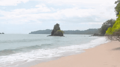 A Beach With A Large Rock In The Middle Of The Water GIF