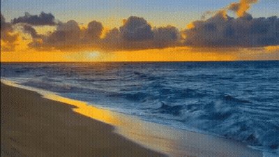 A Beach With A Sunset In The Background And Waves Crashing On The Sand GIF