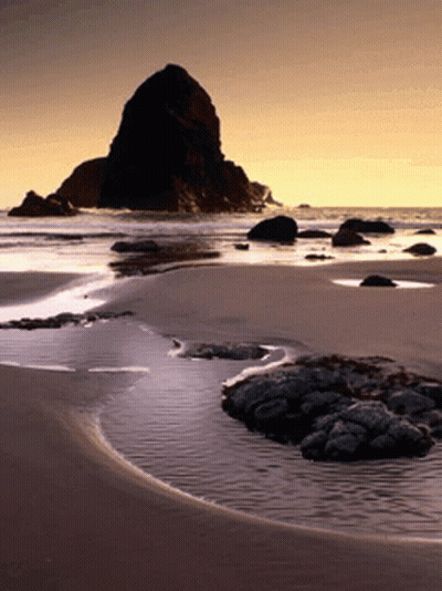 A Beach With Rocks And A Large Rock In The Background GIF