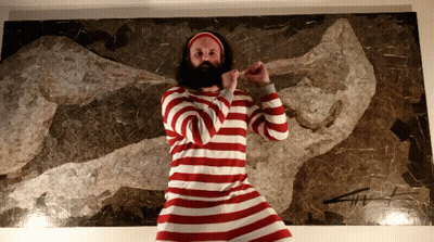 A Bearded Man In A Red And White Striped Shirt Stands In Front Of A Painting GIF