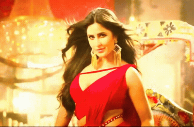 A Beautiful Woman In A Red Dress Is Standing In Front Of A Chandelier . GIF