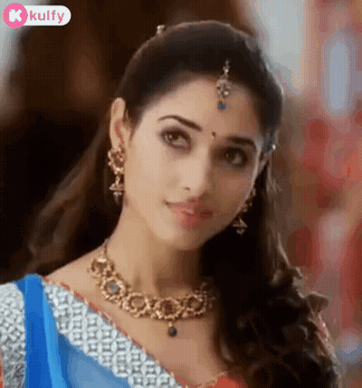 A Beautiful Woman Wearing A Necklace And Earrings Is Looking At The Camera . GIF