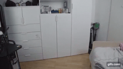 A Bedroom With A Bed , Dressers , And A Vacuum Cleaner . GIF