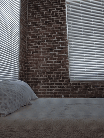 A Bedroom With A Brick Wall And Blinds GIF
