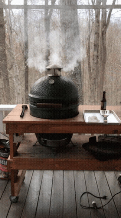 A Big Green Egg Grill Is Smoking A Piece Of Meat On A Wooden Table GIF