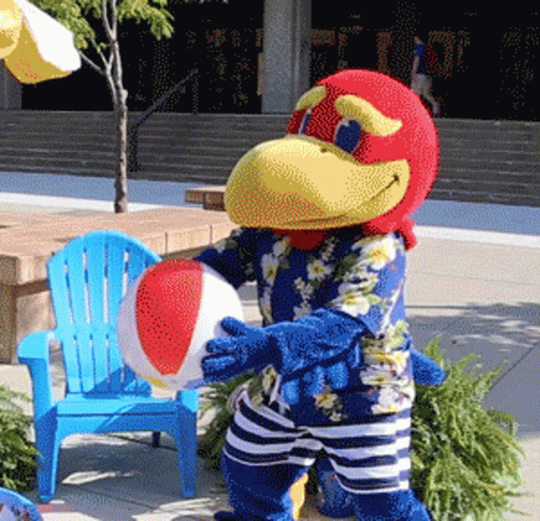 A Bird Mascot Is Holding A Beach Ball In Front Of A Blue Chair GIF