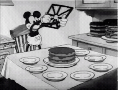 A Black And White Cartoon Of Mickey Mouse Sitting At A Table With A Cake . GIF