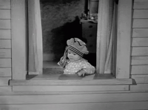 A Black And White Photo Of A Baby Wearing A Hat Looking Out Of A Window GIF