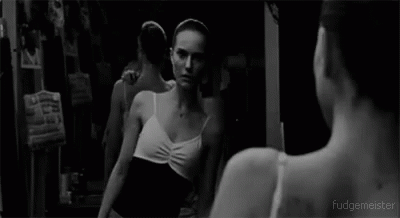 A Black And White Photo Of A Ballerina Looking At Herself In A Mirror . GIF