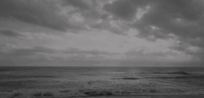 A Black And White Photo Of A Beach With A Cloudy Sky And Waves Crashing On The Shore . GIF