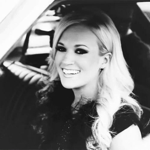 A Black And White Photo Of A Blonde Woman Smiling In A Car GIF