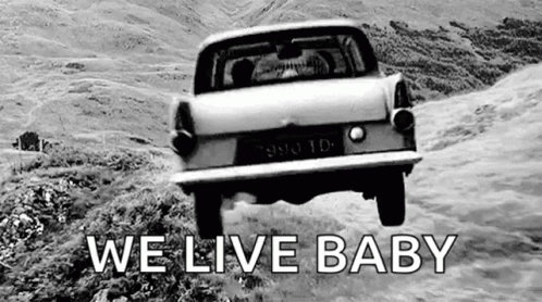 A Black And White Photo Of A Car Driving Down A Hill With The Words `` We Live Baby '' . GIF