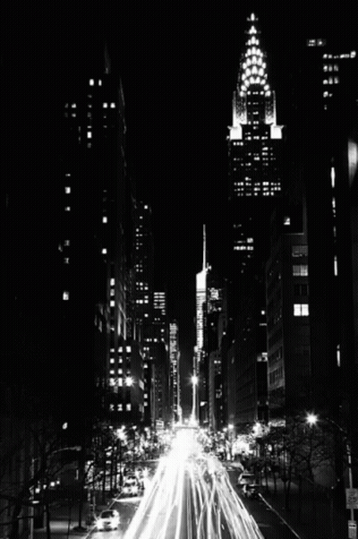 A Black And White Photo Of A City Street At Night With A Tall Building In The Background GIF