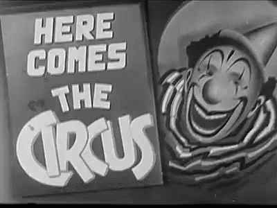 A Black And White Photo Of A Clown And A Sign That Says `` Here Comes The Circus '' GIF