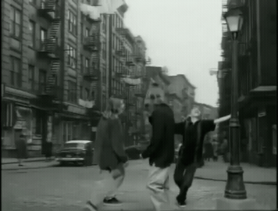 A Black And White Photo Of A Couple Walking Down A Street GIF